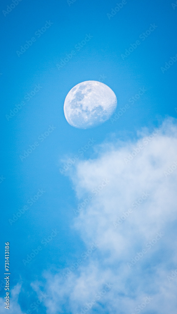 moon in the middle of the day with white clouds around it and a blue sky