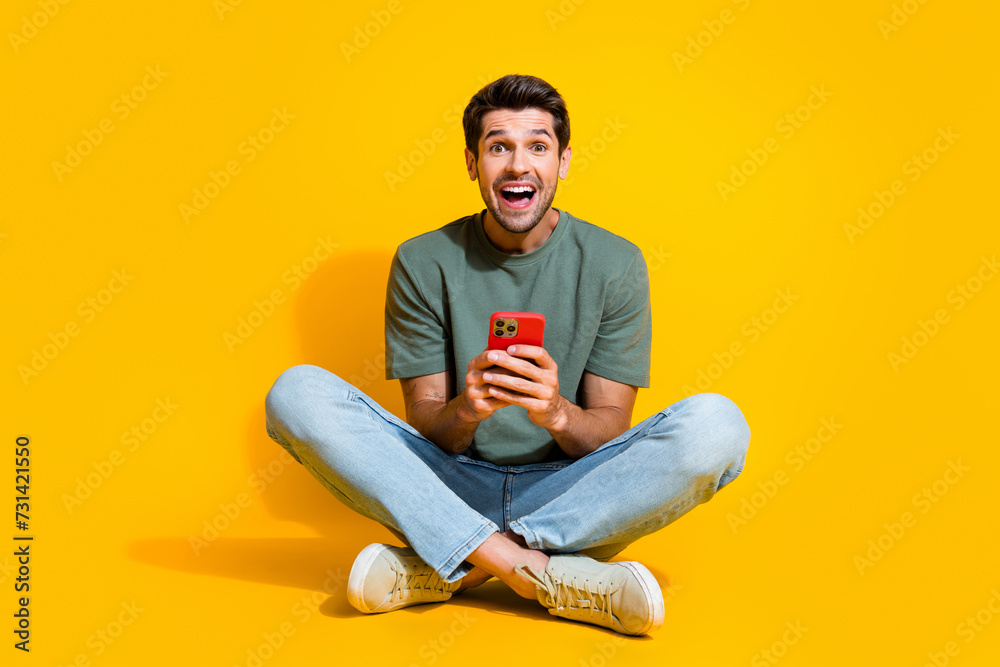 Full length photo of positive impressed guy wear khaki t-shirt communicating modern gadget isolated yellow color background Full length photo of positive impressed guy wear khaki t-shirt communicating modern gadget isolated yellow color background