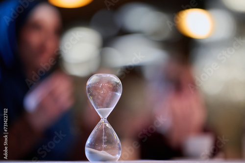 A symbolic hourglass counts down the time to iftar meal, while in the background, an Islamic family devoutly prays, capturing a poignant moment of spiritual connection and anticipation during Ramadan photo