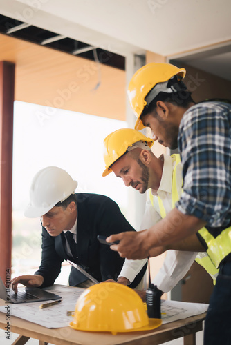 professional engineers in safety vests and hardhats working with blueprints and showing construction, Industrial engineers in hard hat discuss new project, they work in manufacturing factory.