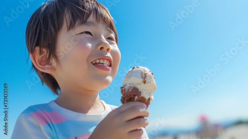 3 year old Asian boy enjoying a melting chocolate ice cream on a sweltering hot summer day. Clear blue summer sky in background