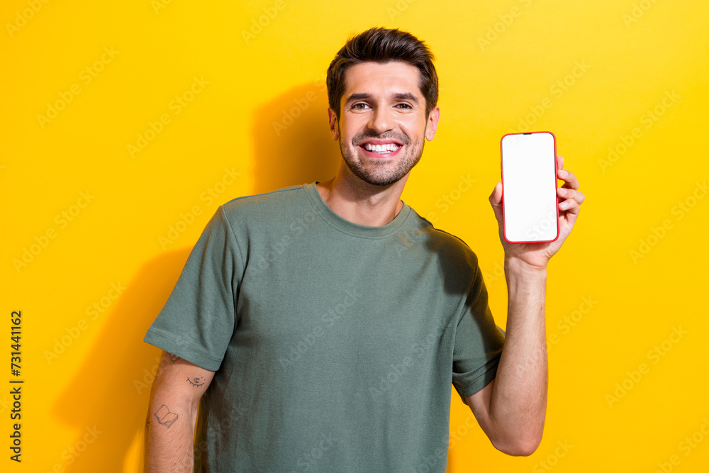 Portrait of satisfied smart guy wear stylish t-shirt demonstrate smartphone screen menu empty space isolated on yellow color background Portrait of satisfied smart guy wear stylish t-shirt demonstrate smartphone screen menu empty space isolated on yellow color background