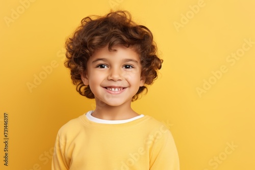 Portrait of happy little boy with curly hair looking at camera over yellow background