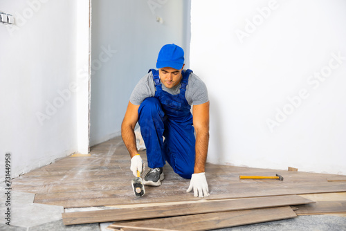 Repairman in overall laying parquet on floor during home improvement works in apartment.