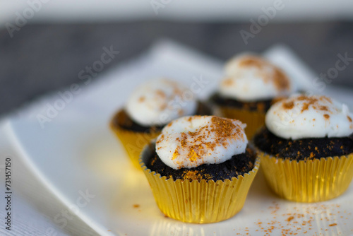 Chocolate cupcakes with white marshmallow icing, real edible gold leaf sprinkles in a gold cupcake wrapper on a white plate with room for text in the image - 4 cupcakes wide