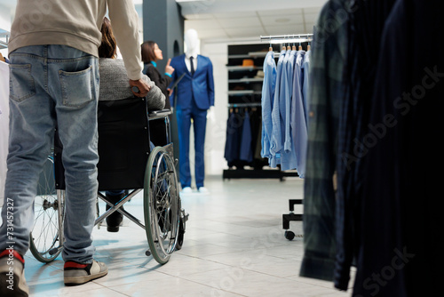 African american woman in wheelchair getting help while shopping for apparel in clothing store. Fashion boutique client with physical disability choosing casual outfit in mall