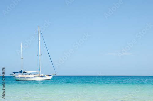 One white yacht with tall masts on blue water with clear blue sky. Seascape. Queensland, Australia. No people.