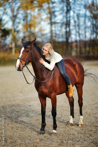 Young blonde girl with her brown horse on the riding arena in portraits.