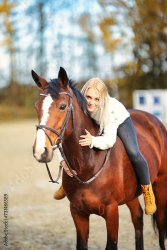 Young blonde girl with her brown horse on the riding arena in portraits.