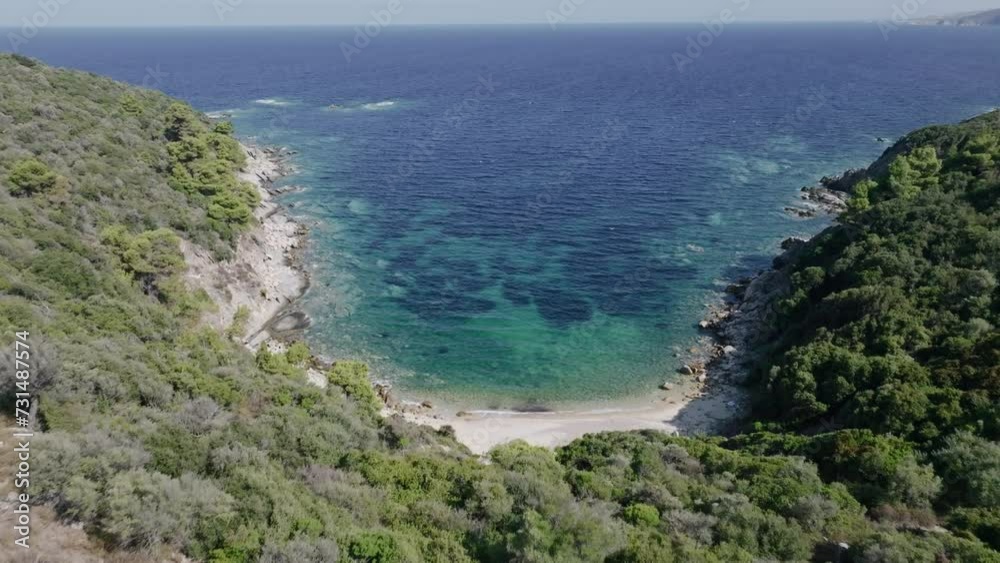 Aerial shot of a drone flying forward over a secluded bay, where crystal clear waters meet a rocky shore fringed by green foliage Aerial shot of a drone flying forward over a secluded bay, where crystal clear waters meet a rocky shore fringed by green foliage