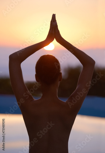 Tree, yoga and woman meditate at sunset by swimming pool for healthy body, wellness and zen outdoor. Rear view, vrikshasana pose and person at water at twilight to relax, peace or calm for balance