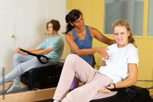 Pilates instructor helping teen boy and girl do hand stretch on the machine in the gym