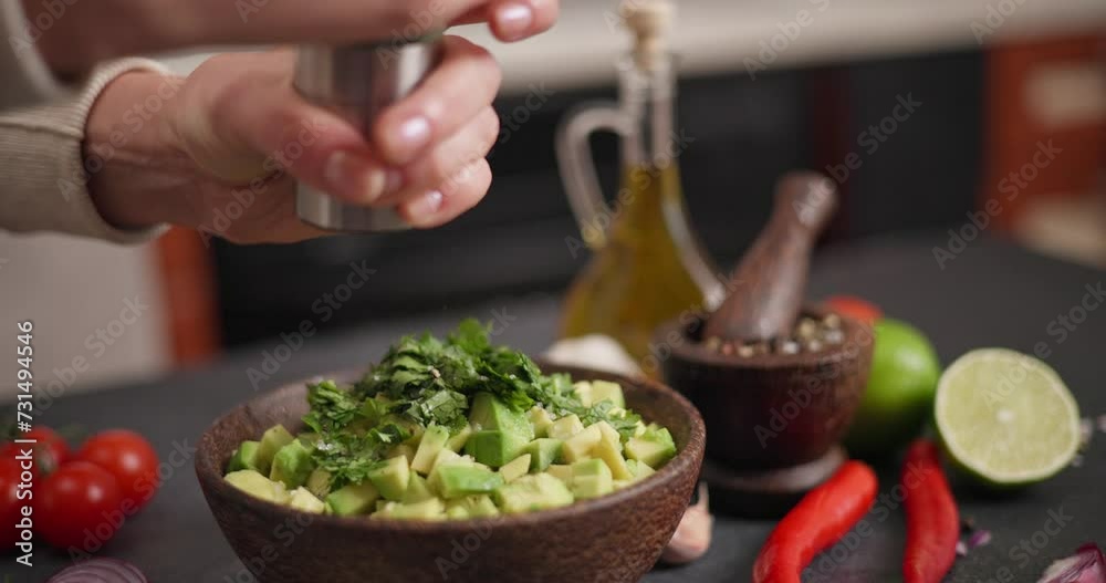 Salsa recipe - Woman pouring grinded pepper onto ingredients in wooden bowl - avocado, onion and cilantro Salsa recipe - Woman pouring grinded pepper onto ingredients in wooden bowl - avocado, onion and cilantro