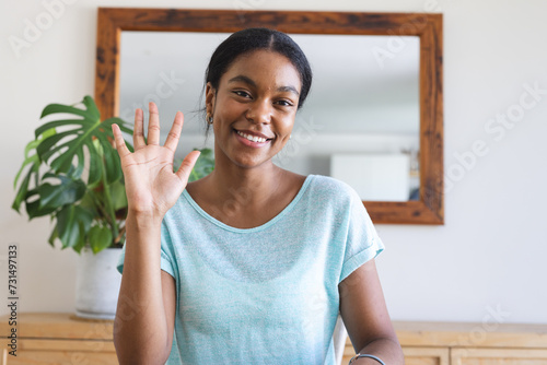 Young biracial woman waves cheerfully in a home setting on a video call