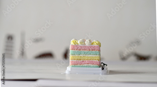 Closeup of Beautiful Pastel Rainbow Cake and a black plastic fork on white wooden table with blurred bokeh background at Thailand.