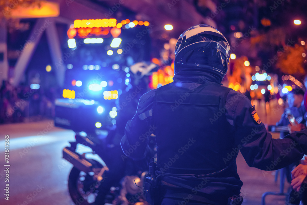 Back View Of A Traffic Police Motorcyclist In The City At Night With Siren Lights. Concept Of Road Safety, Traffic, Accident, Citizen Help And Urban Police. Back View Of A Traffic Police Motorcyclist In The City At Night With Siren Lights. Concept Of Road Safety, Traffic, Accident, Citizen Help And Urban Police.