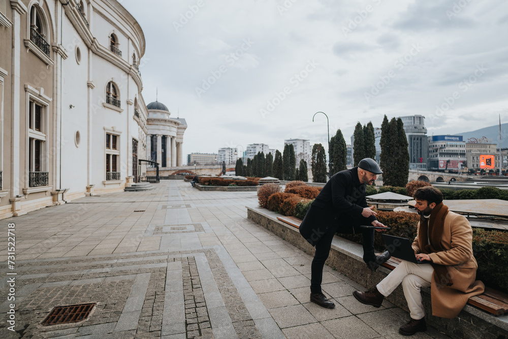 Two professional men engaged in a business conversation while using a laptop outside, with classical architecture and cityscape in the background.