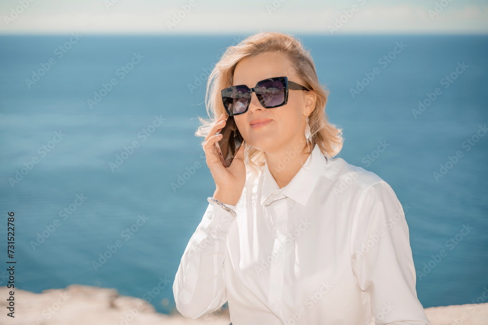 Freelance women sea working on a computer. Pretty middle aged woman with computer and phone outdoors with beautiful sea view. The concept of remote work. Freelance women sea working on a computer. Pretty middle aged woman with computer and phone outdoors with beautiful sea view. The concept of remote work.