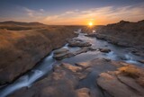 Majestuoso Paisaje remoto rio salvaje rodeado de rocas al atardecer , el sol ocultandose en el horizonte.