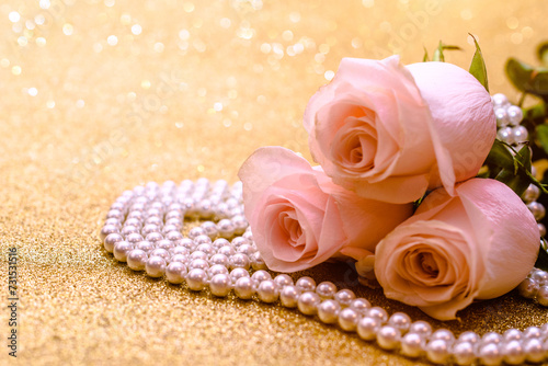 Pink rose and pearl necklace on a shiny gold background
