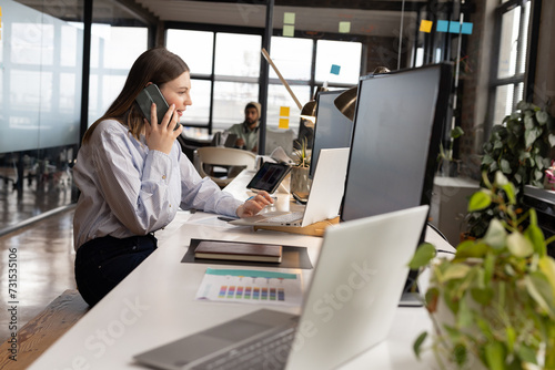 Young Caucasian woman talks on the phone in a casual business setting in a modern office photo