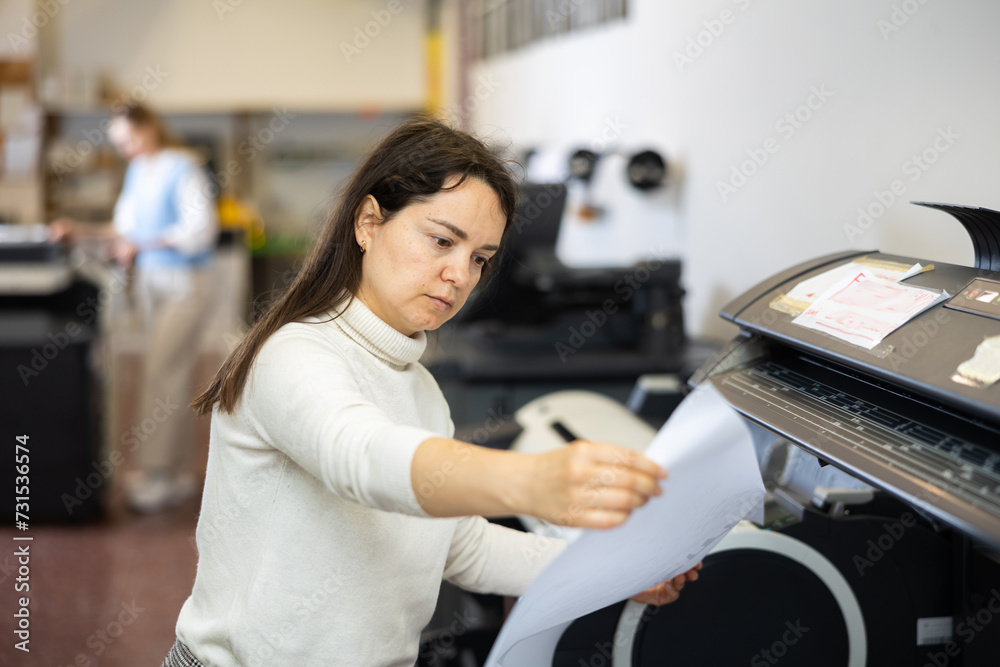 Woman employee of printing house works on a modern printer