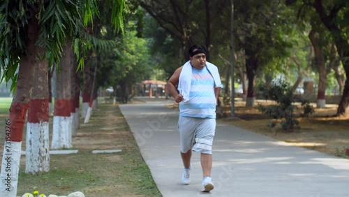 Indian man gets tired after a morning jog - healthy lifestyle  sweating  overweight  summer morning. Obese man running in the park - running track  outdoor workout  out of breath  persistent motiva... photo