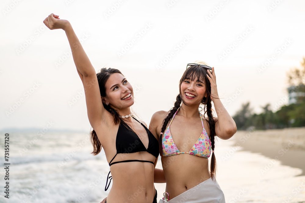 Portrait of two young women friends in bikini standing in the beach.  