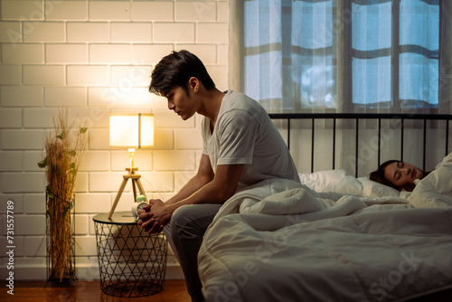 Asian frustrated insomnia man in pajamas sit on bed in dark night time.  photo