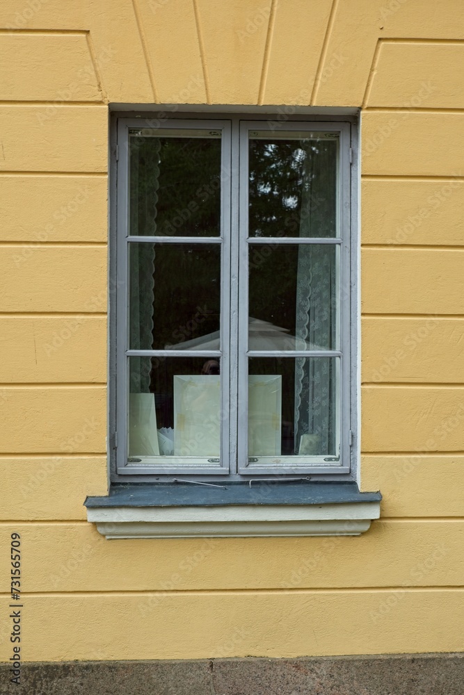 Fototapeta premium Window with with grey frame on a yellow painted stone wall.