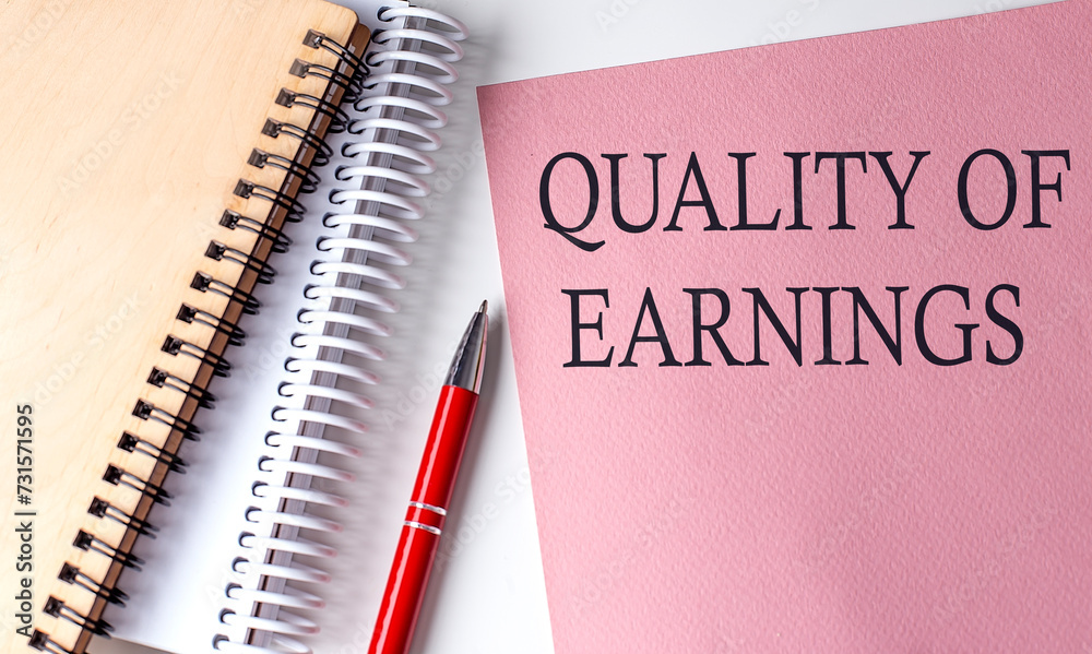 QUALITY OF EARNINGS word on the pink paper with office tools on white background