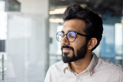 Man with black hair, glasses & beard smiles while looking out window