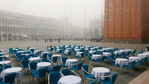 Venice in winter fog. Unused restaurant seating in Piazza San Marco, St Mark's Square with Campanile and Basilica.