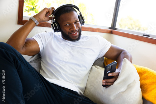 Smiling Black Guy With Headphones And A Phone relaxes in couch In A Stunning Interior. Looking At Camera. Tecnologi Concept