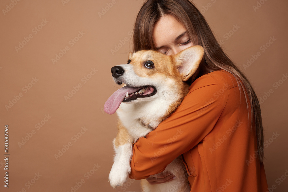 Girl hugging Pembroke Welsh Corgi on a beige clean background in the studio, love for animals Girl hugging Pembroke Welsh Corgi on a beige clean background in the studio, love for animals