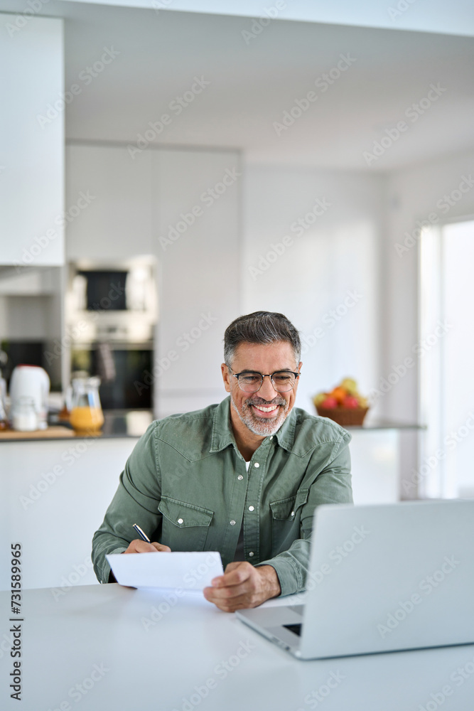Happy middle aged mature senior man entrepreneur looking at paper bill checking financial invoice or tax document making online household payments working on laptop at home kitchen table. Vertical Happy middle aged mature senior man entrepreneur looking at paper bill checking financial invoice or tax document making online household payments working on laptop at home kitchen table. Vertical