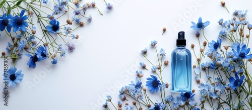 A plastic bottle filled with liquid perfume, standing on a white table surrounded by vibrant blue flowers.