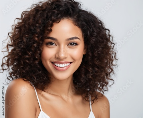 Close up studio shot of beautiful young mixed race woman model with curly dark hair looking at camera with charming cute smile 