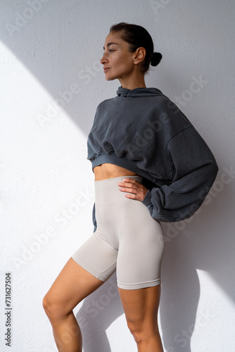 beautiful athletic brunette in short leggings and a sweatshirt. fitness model in sportswear on a light background. fitness motivation