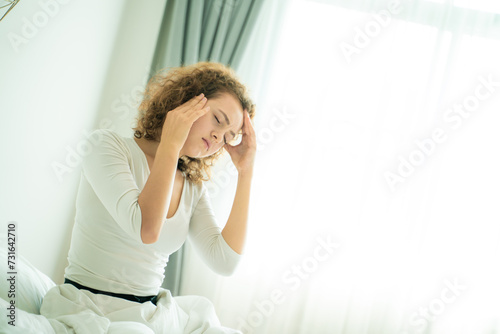 Young women sitting on bed wake up holding her head feel sick