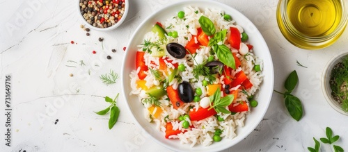 Fresh vegetable rice salad with bell pepper, tomato, green peas, black olives, and olive oil, served on a white table directly above.