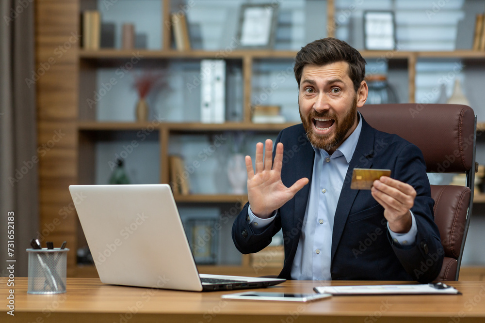 Excited mature businessman in a suit makes an unexpected discovery with a credit card at a home office desk. Excited mature businessman in a suit makes an unexpected discovery with a credit card at a home office desk.
