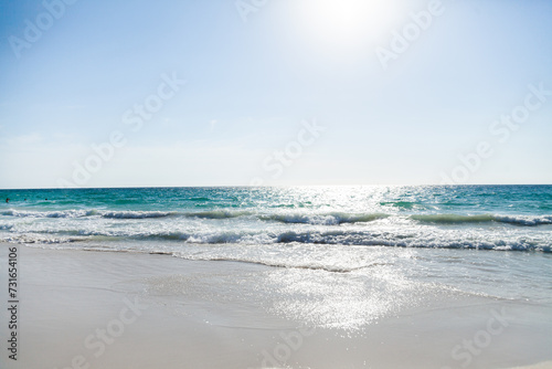 Sunlight sparkling on clear waters of the sea as waves wash the sand photo
