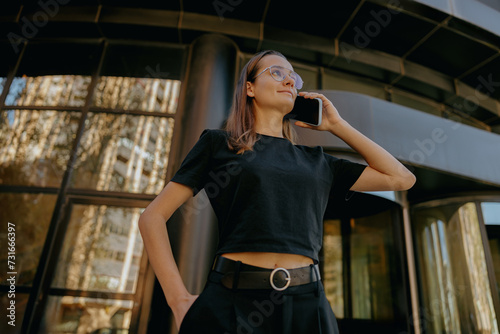 Young woman manager is talking mobile phone whiile standing on modern building background photo