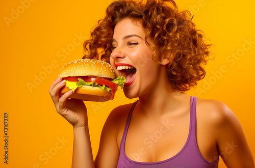 Portrait of a woman eating a delicious cheeseburger on a colored background.