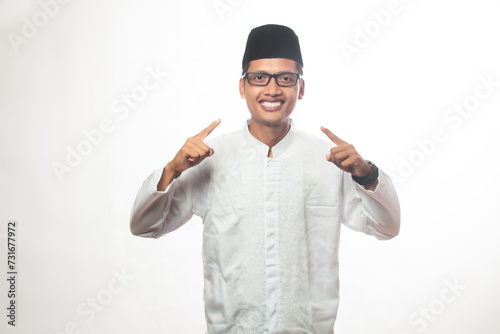 Asian Muslim man with glasses, brown skin, smiling facing the camera and both hands pointing forward, Muslim man wearing koko shirt. white isolated