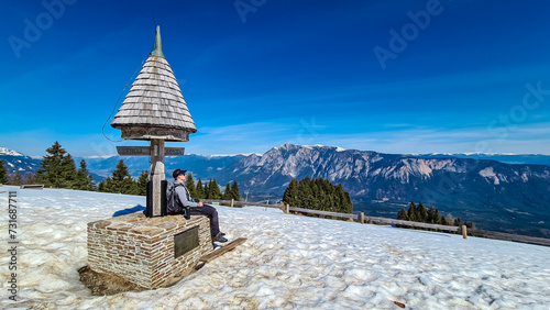 Hiker man at wooden monument at Dreilaendereck, Karawanks, Carinthia, Austria. Triangle border corner of Austria, Slovenia and Italy. Hiking in remote alpine landscape in springtime, Austrian Alps photo