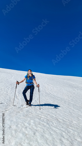 Hiker woman walking on snow covered meadow at idyllic Dreilaendereck, Karawanks, Carinthia, Austria. Clear blue sky in European Alps in early spring. Hiking in remote alpine landscape in springtime