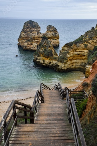 Wooden bridge situated next to a beach near some rocky formations and the vast ocean