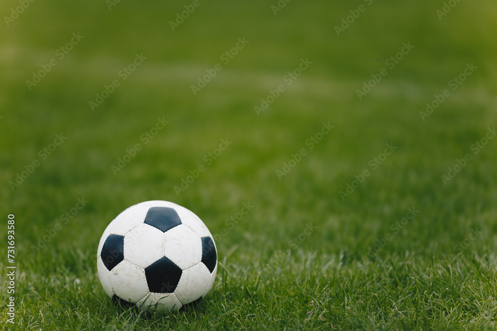 Classic Soccer Ball on Training Pitch. Football Natural Grass Turf. Soccer Stadium in Blurred Background. Young Players Exercising in the Background Classic Soccer Ball on Training Pitch. Football Natural Grass Turf. Soccer Stadium in Blurred Background. Young Players Exercising in the Background